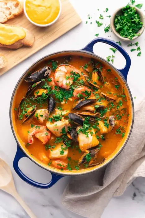 Bouillabaisse i en blå gryta. Man kan tydligt se både räkor och musslor och fiskbitar.